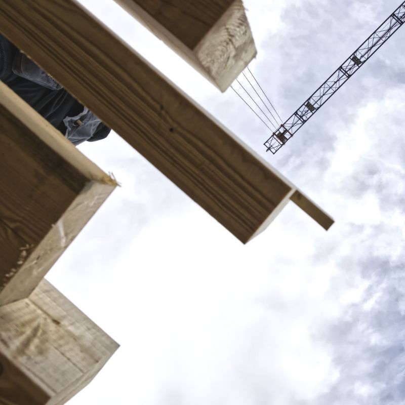 Holzbalken eines Dachstuhls von unten, im Hintergrund ein Kran